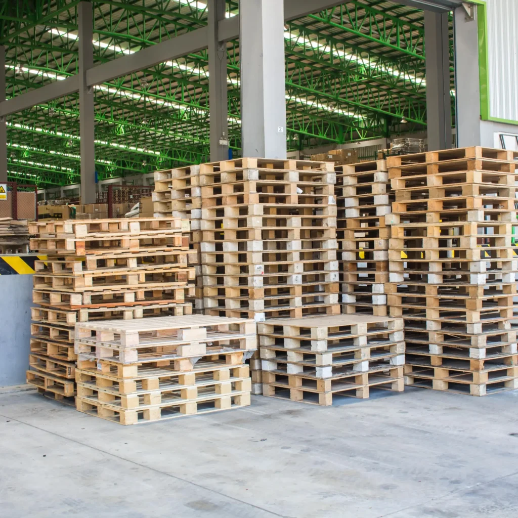 Stosy drewnianych palet ułożonych w magazynie. Palety gotowe do dalszego transportu i użycia w procesach logistycznych.