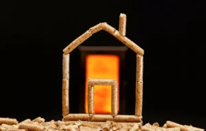 Dom zbudowany z pelletów drzewnych na tle płomienia w piecu, symbolizujący ogrzewanie biomasa.