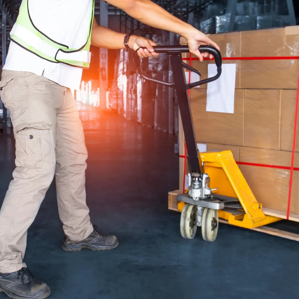 Pracownik transportuje palety w magazynie przy pomocy wózka paletowego. Proces załadunku towarów na paletach w przestrzeni magazynowej.