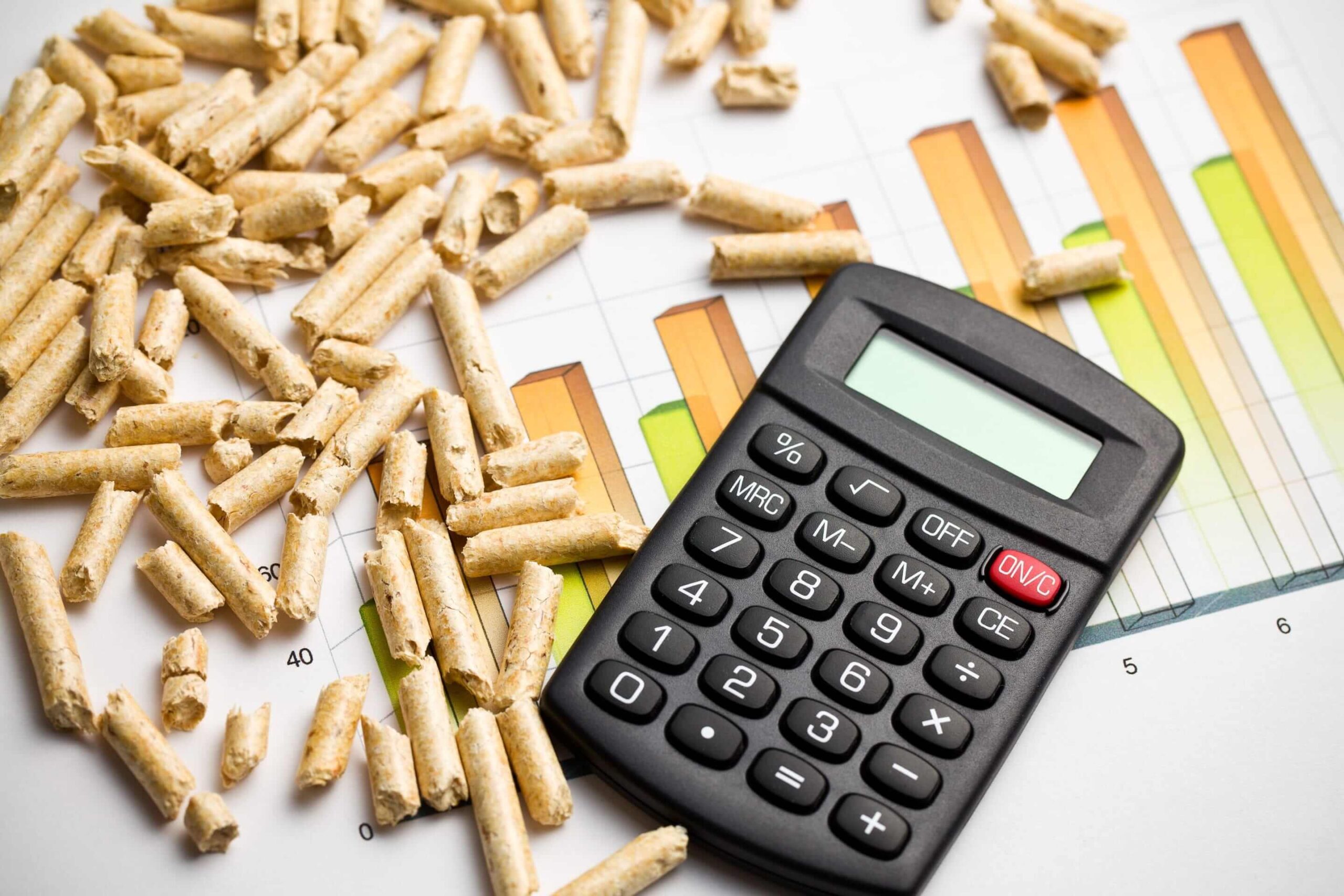 Rozsypany pellet drzewny na kartce ze słupkami, obok kalkulator.