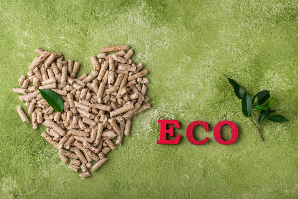 UÅ‚oÅ¼one serce z rozsypanego pelletu drzewnego obok czerwony napis ECO oraz zielone listki na oliwkowym tle.