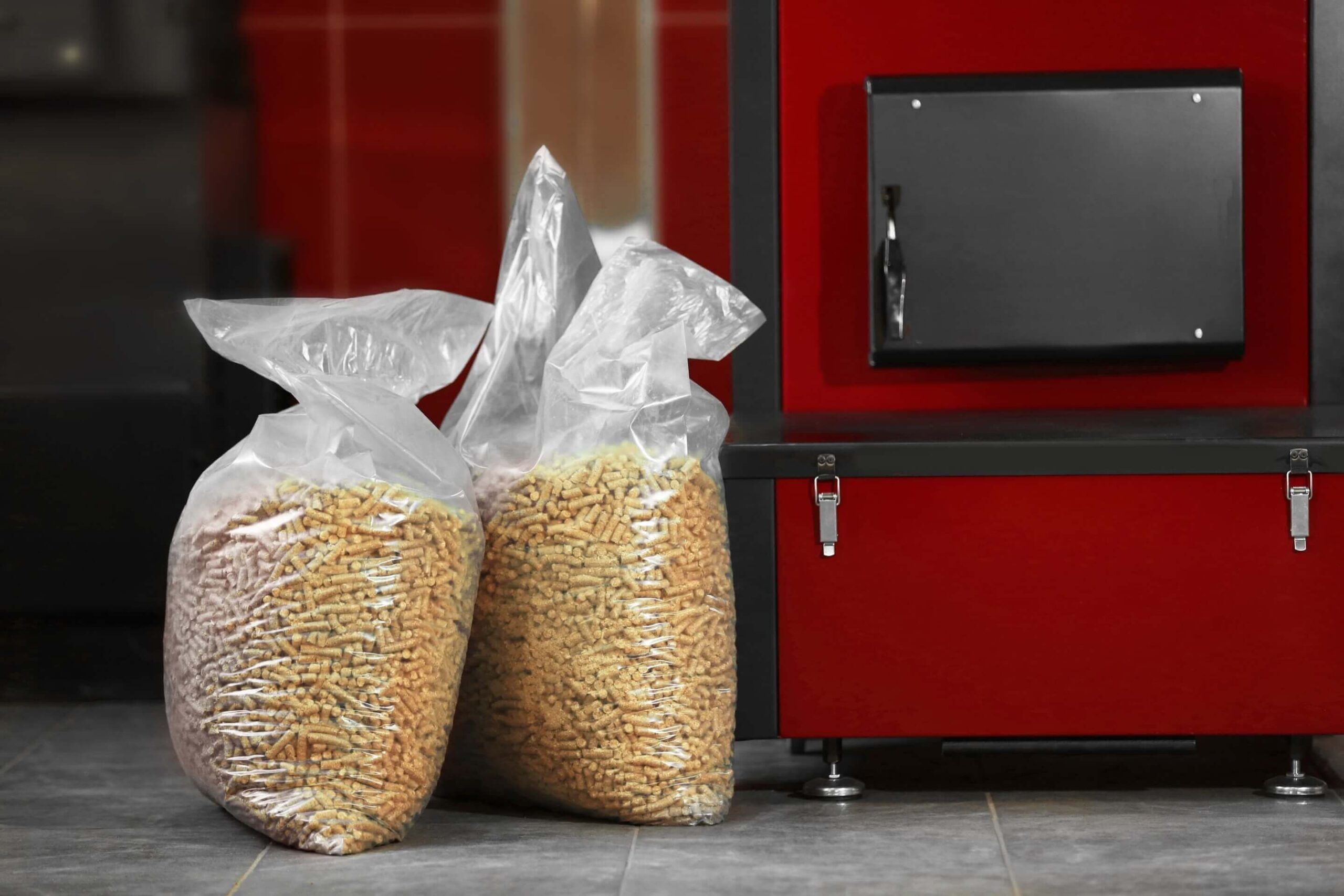 Dwa worki pelletu drzewnego obok czerwonego pieca na pellet.