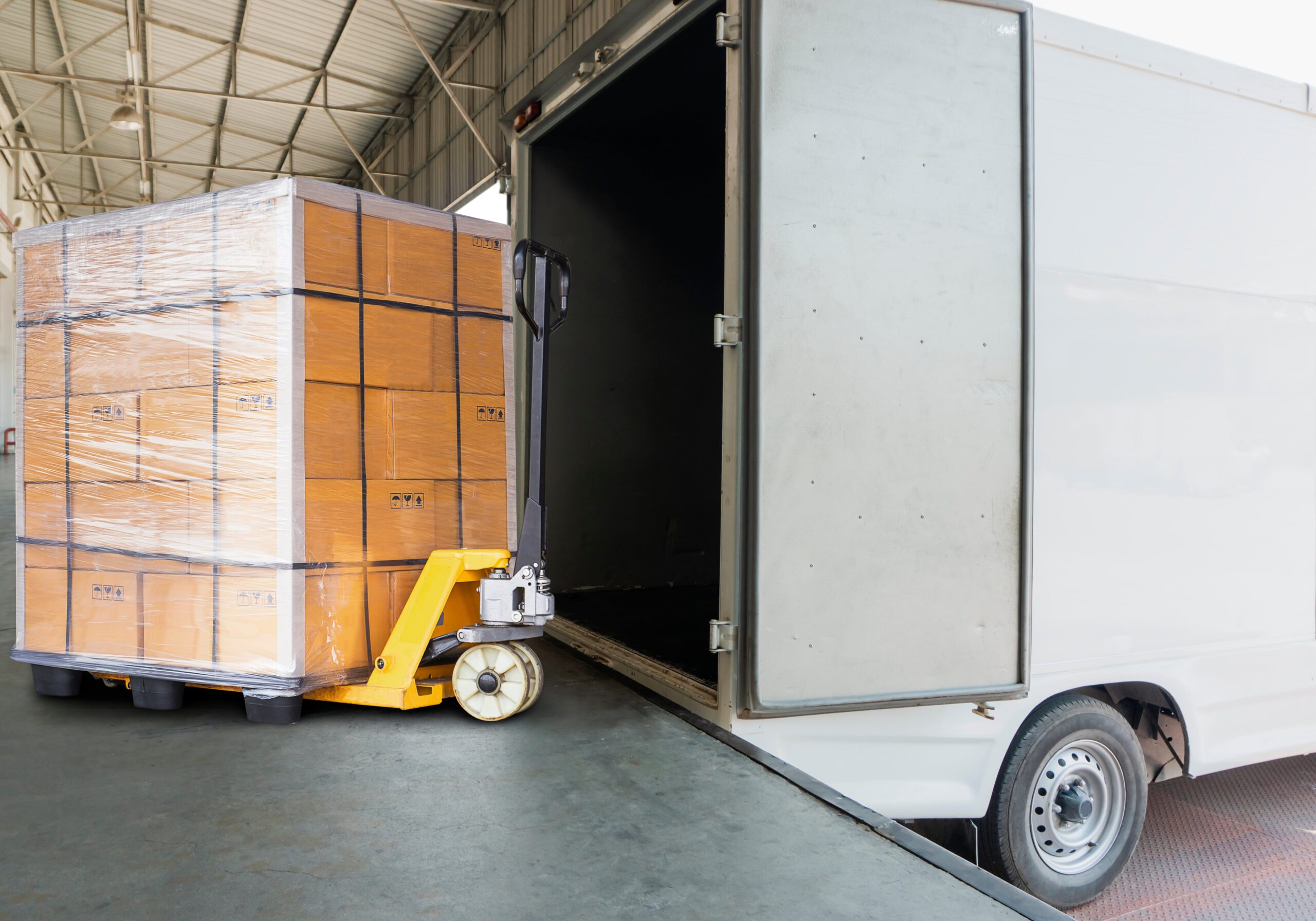 Paleciak z załadowaną paletą wjeżdża do ciężarówki. Zdjęcie przedstawia proces załadunku towarów do pojazdu transportowego w magazynie Kampol.